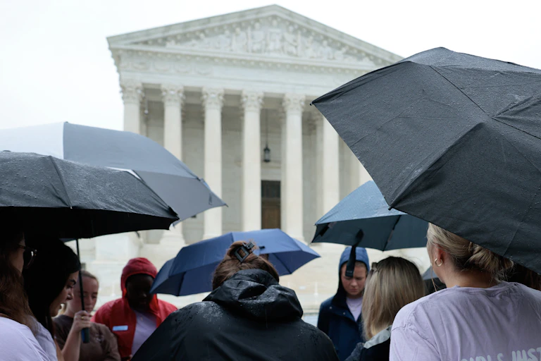 Several people holding umbrellas stand in front of a federal building with white columns.