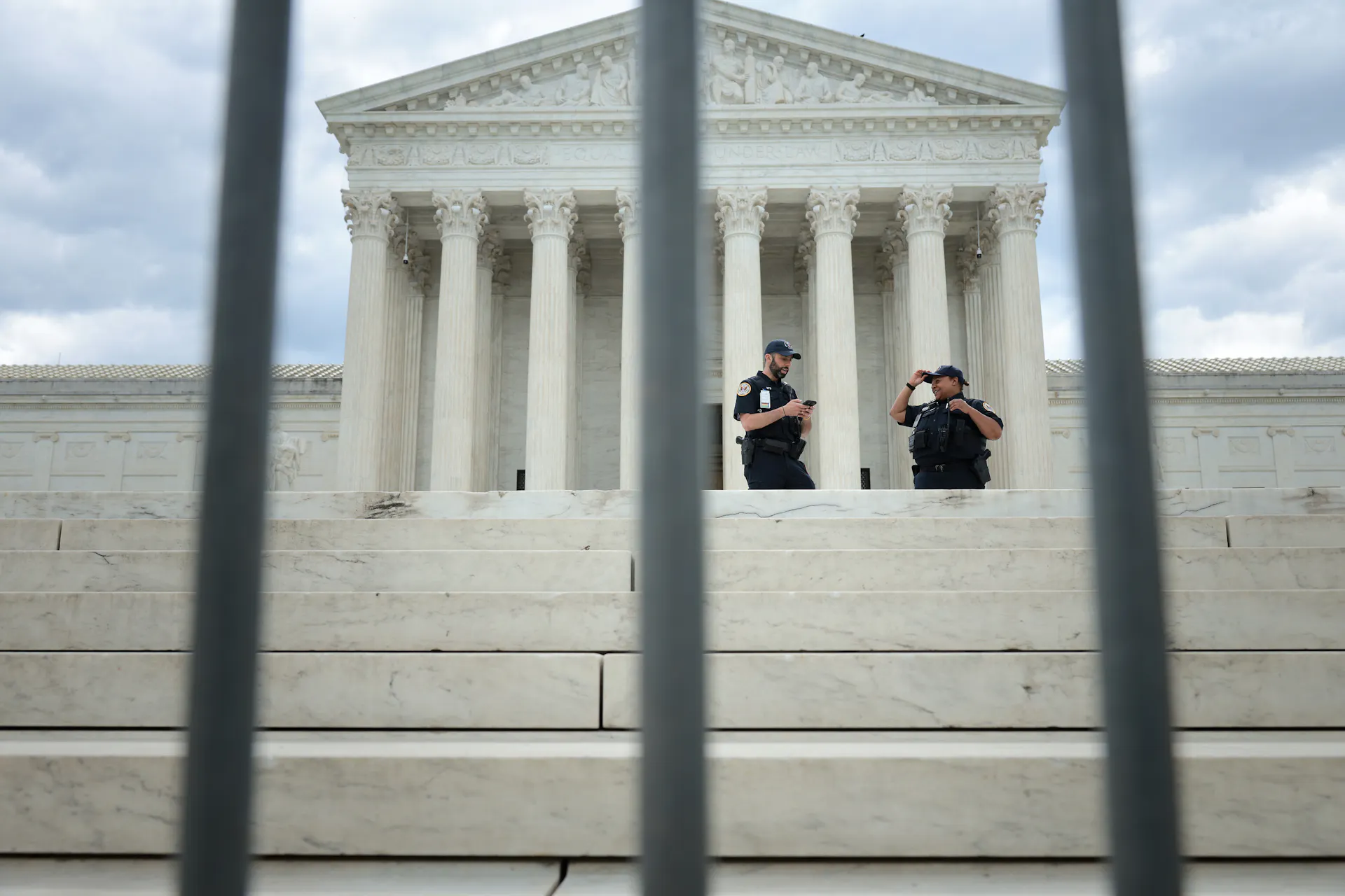 Two policemen seen standing behind bars stand in front of a federal building.