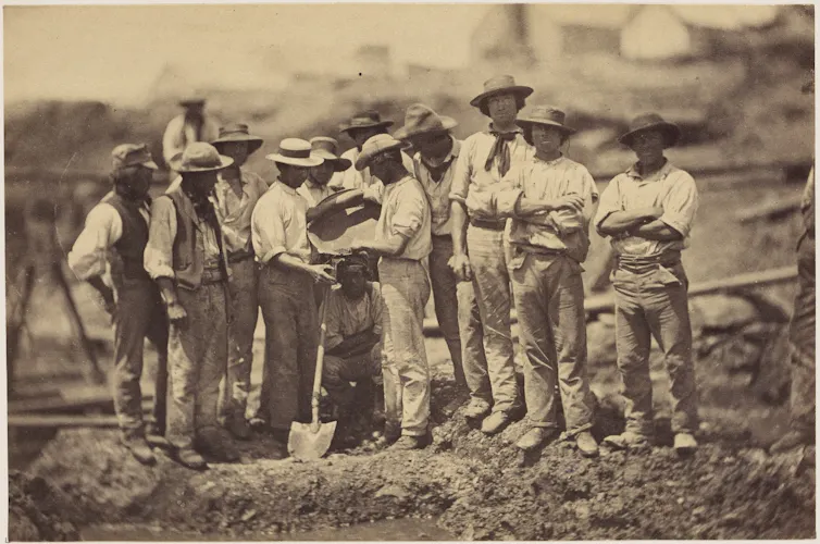 A historical black and white photo of a group of men prospecting for gold.