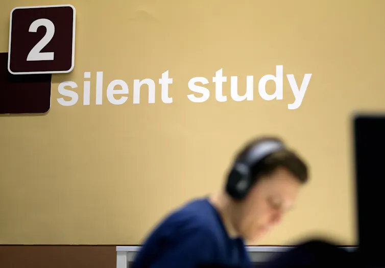 A man wears headphones and sits looking down in a room that has the words 'Silent study,' and the number 2 on the wall.
