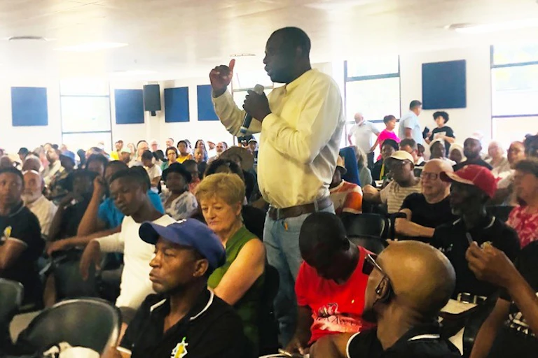 Standing man speaks with a microphone in a room full of seated people
