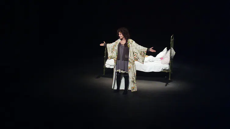 A woman on a stage, arms outspread, in a spotlight.