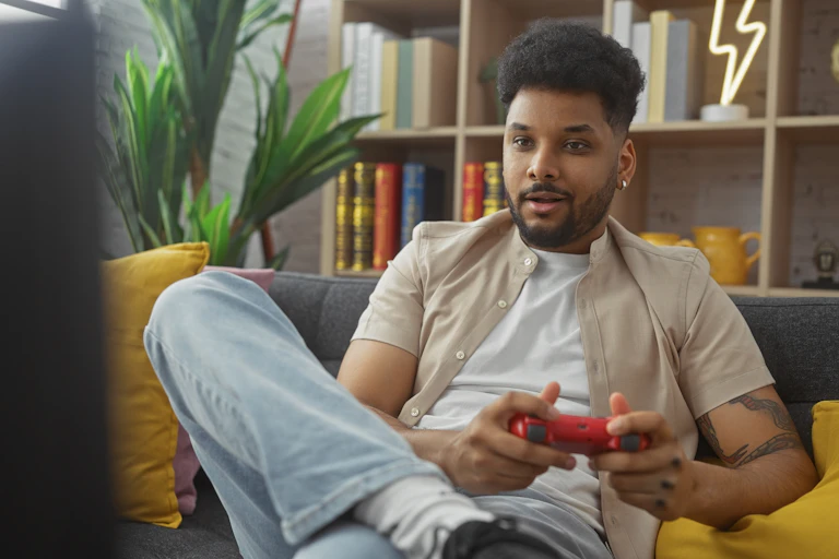 man sat on yellow sofa, playing video game, hand held red console