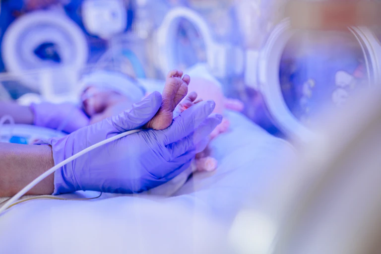 Close up of maternity unit staff holding the hands and legs of a newborn in a medical incubator under ultraviolet lamp in a neonatal intensive care unit.