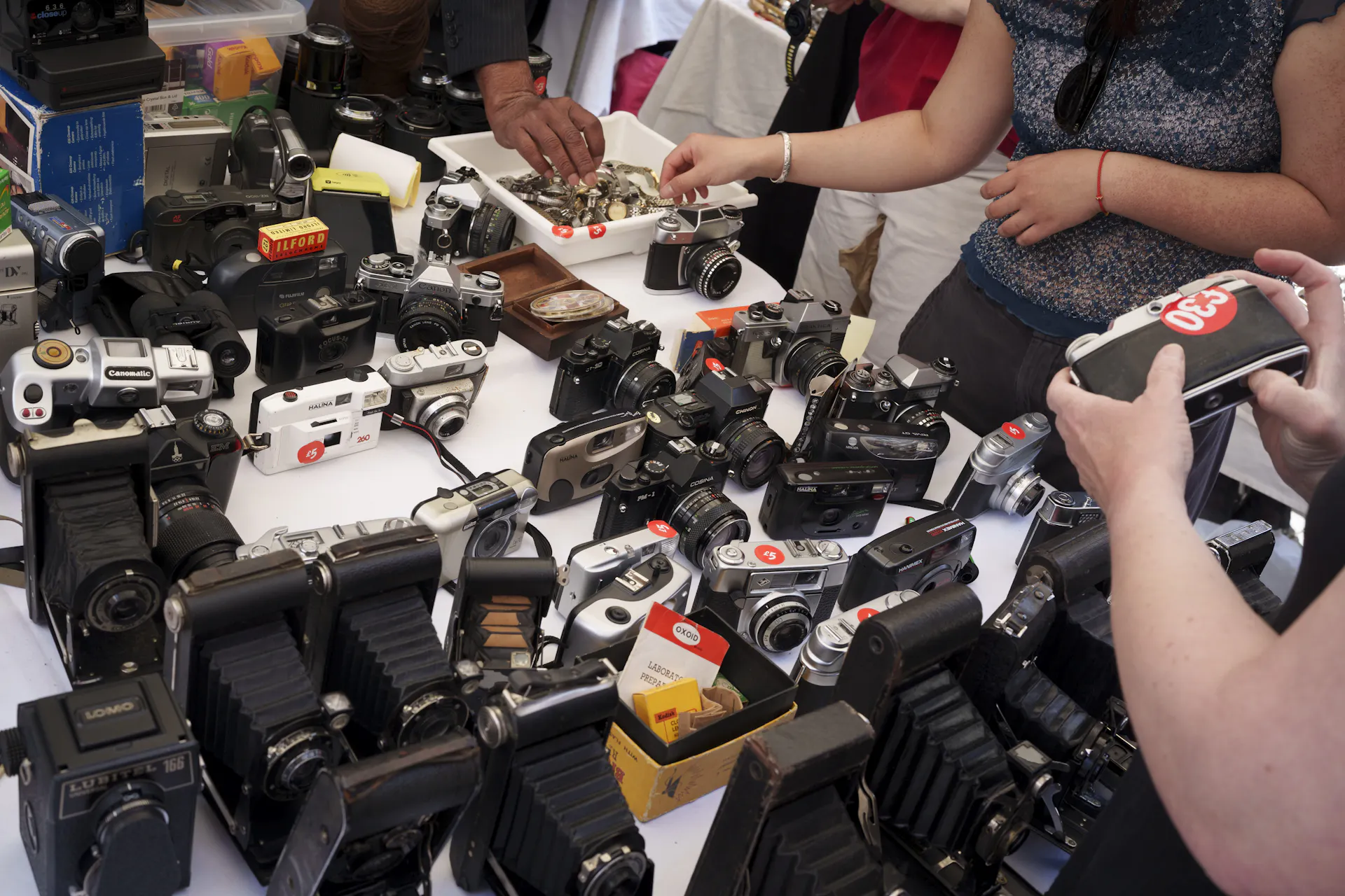 A table featuring an array of camera equipment spanning different eras, with hands holding some of the objects.
