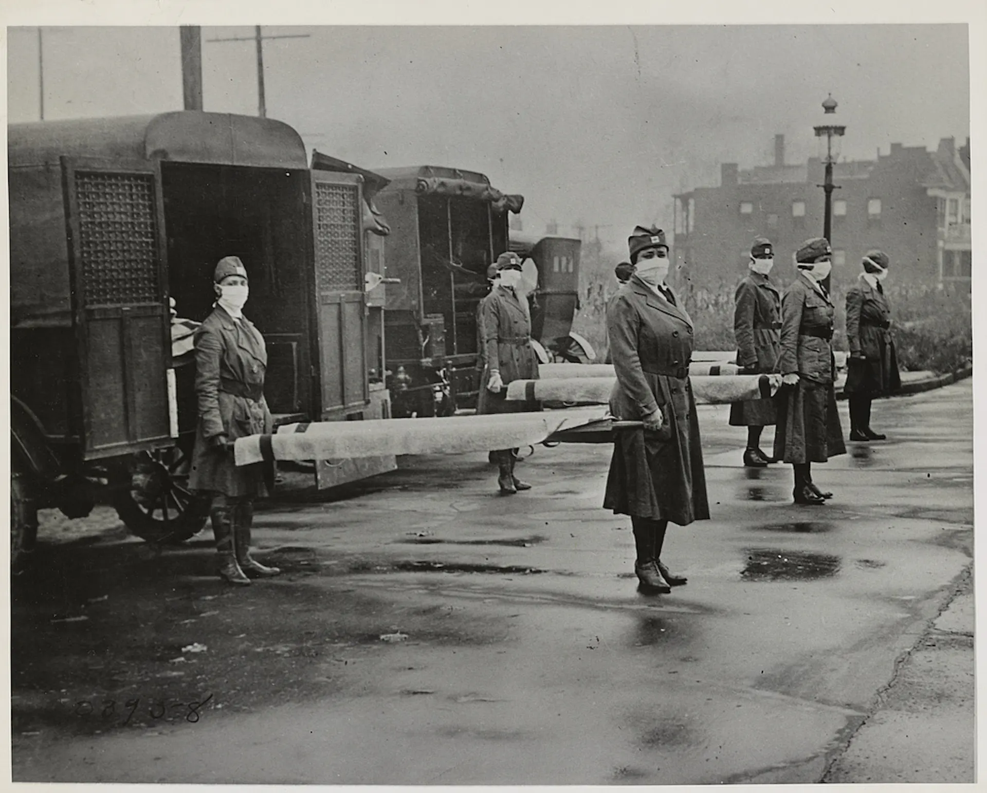 Mark-wearing nurses holding stretchers in front of military ambulances in a black and white photo from the 1918 flu pndemic
