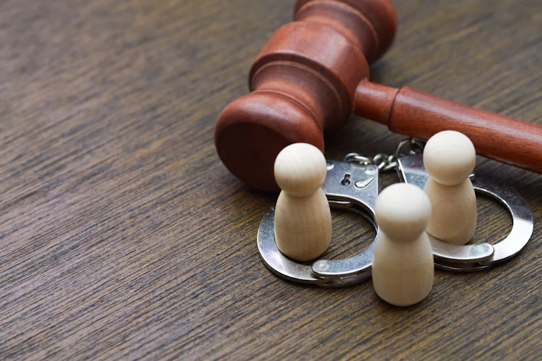 Tres figuras de madera con unas esposas y un mazo