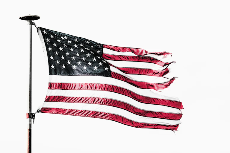 A tattered American flag flies from a flagpole.