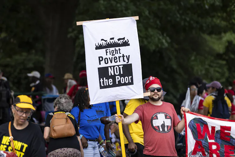 An activist holds a sign that says 'Fight Poverty, Not the Poor' during a rally.