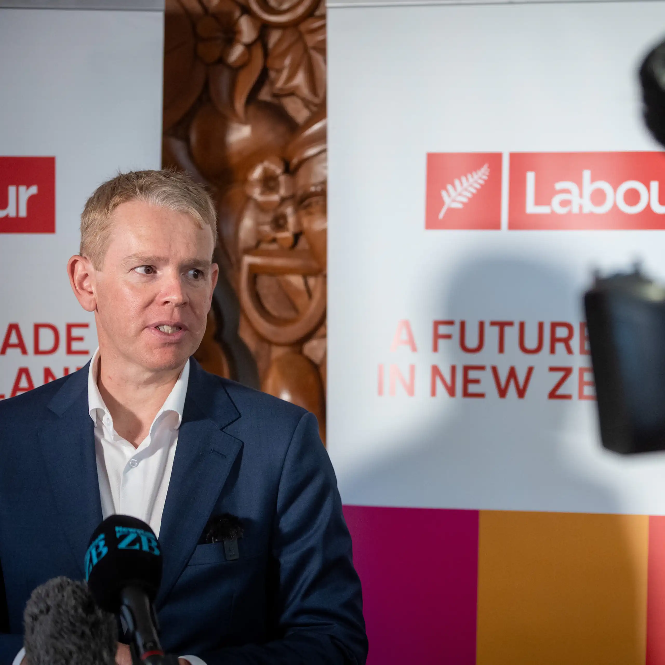 Chris Hipkins speaks to the media in front of a Labour campaign poster