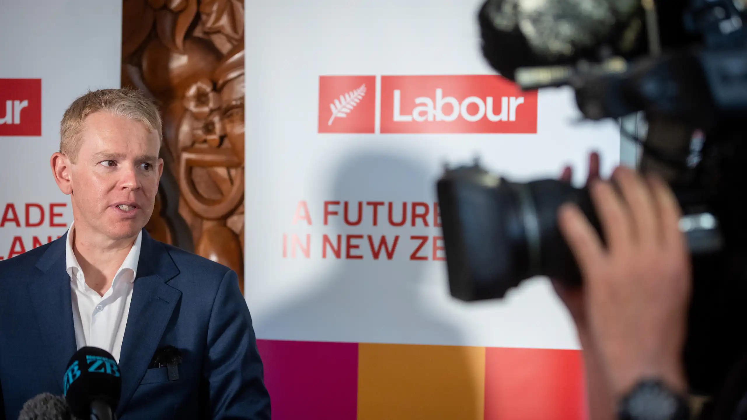 Chris Hipkins speaks to the media in front of a Labour campaign poster