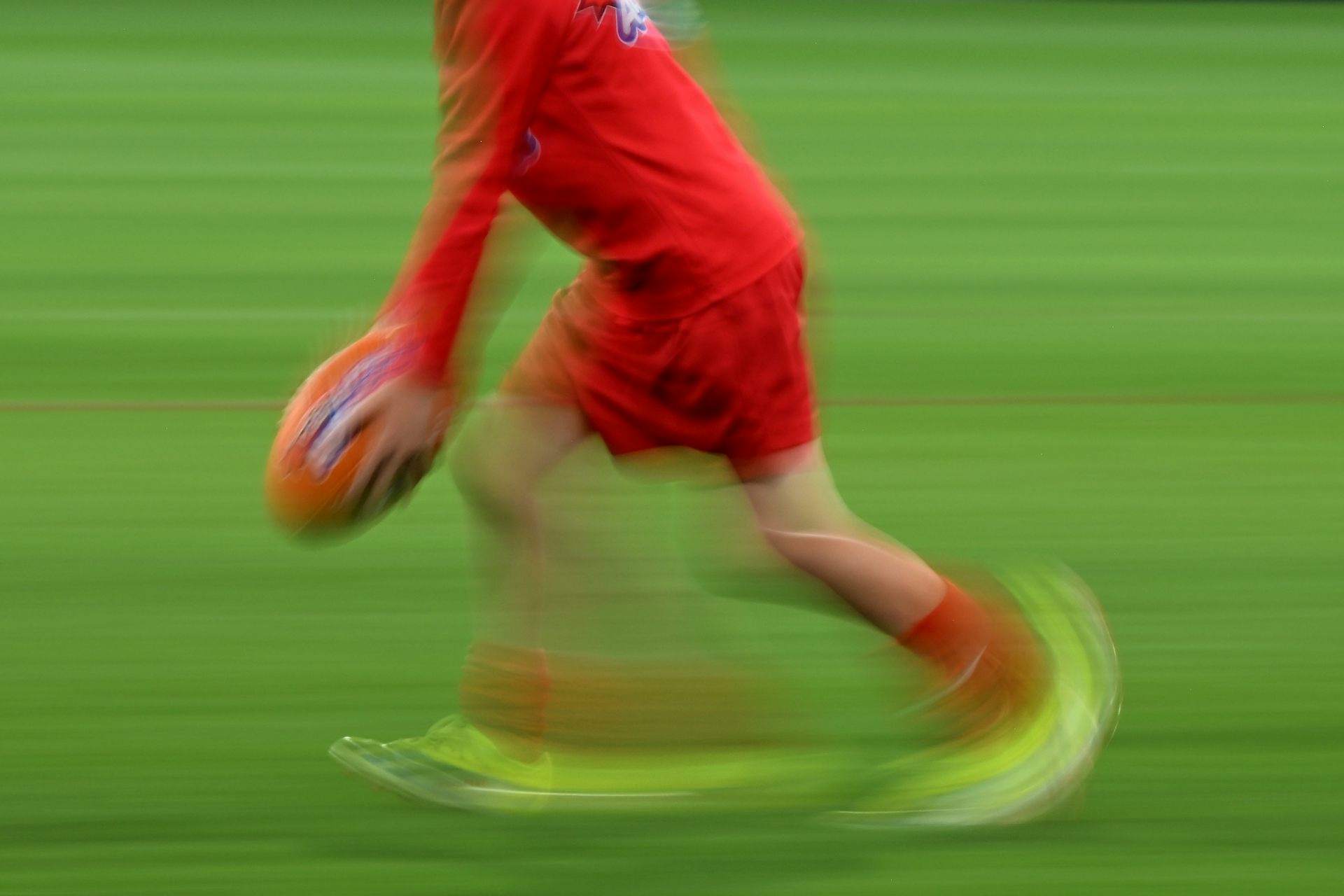 A blurred image shows a child kicking a footy ball.
