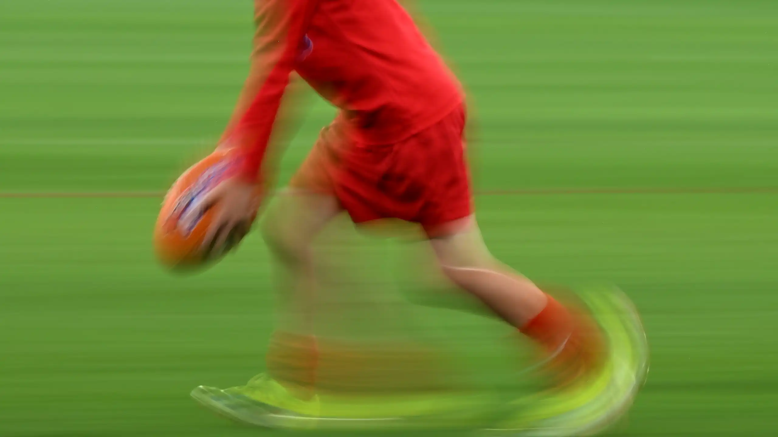 A blurred image shows a child kicking a footy ball.