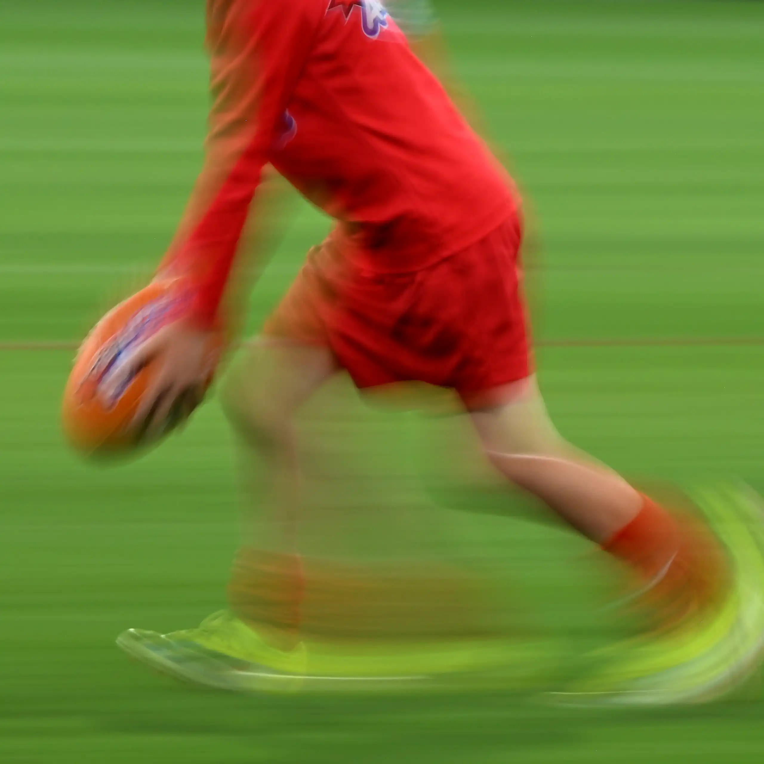 A blurred image shows a child kicking a footy ball.