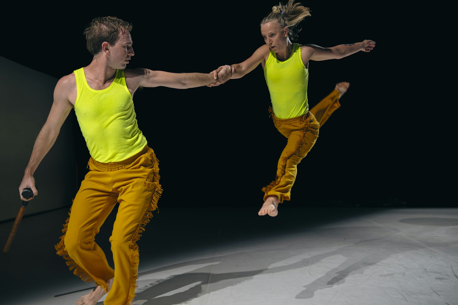 A woman jetés, holding a man's hand.
