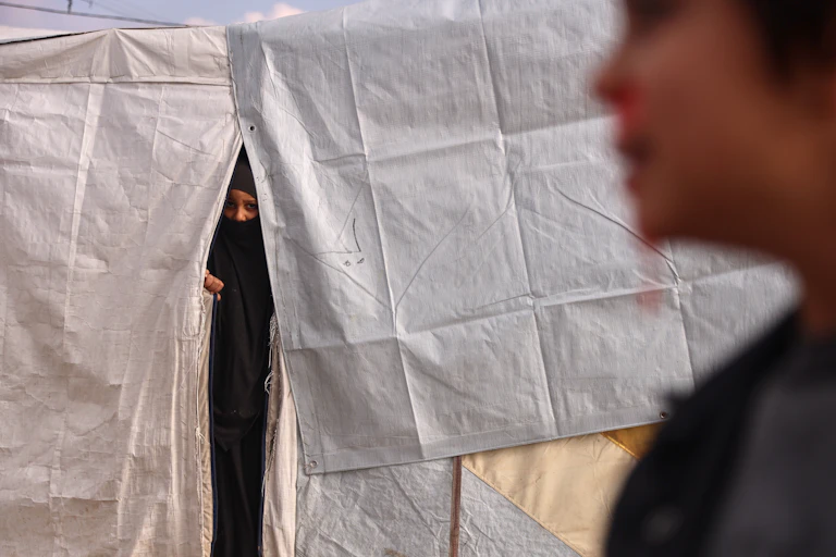 A woman in a niqab peers out of a white tent
