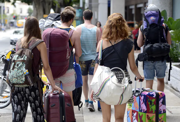 The backs of a group of tourists with large backpacks and suitcases