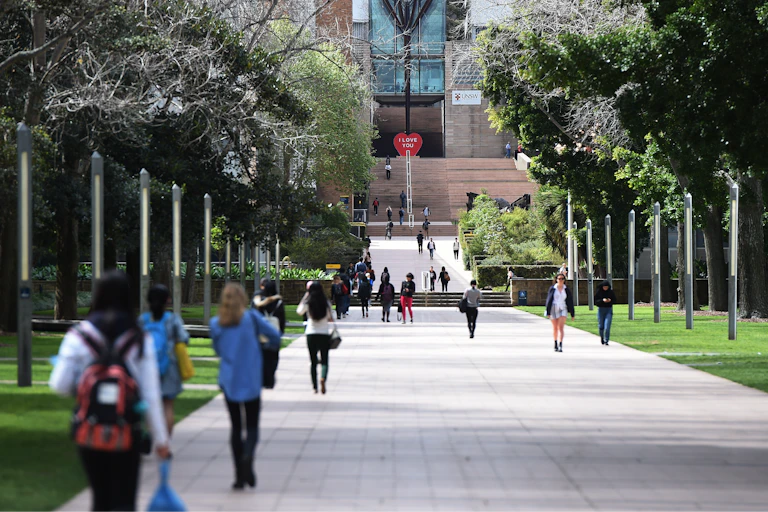 Students walk towards a university building in the distance while others walk away from it towards the camera.