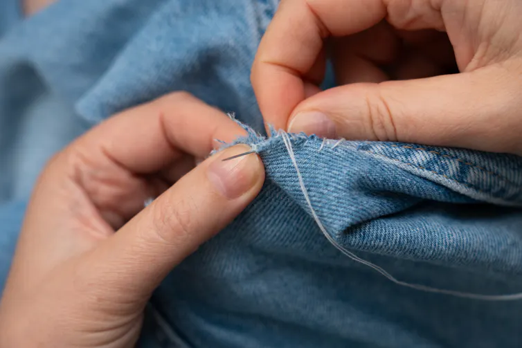 woman's hands sewing and mending blue denim jeans with needle and thread