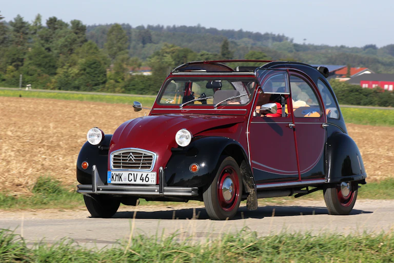 Deux chevaux Citroën modèle Charleston (bordeaux et noir) sur une route de campagne.