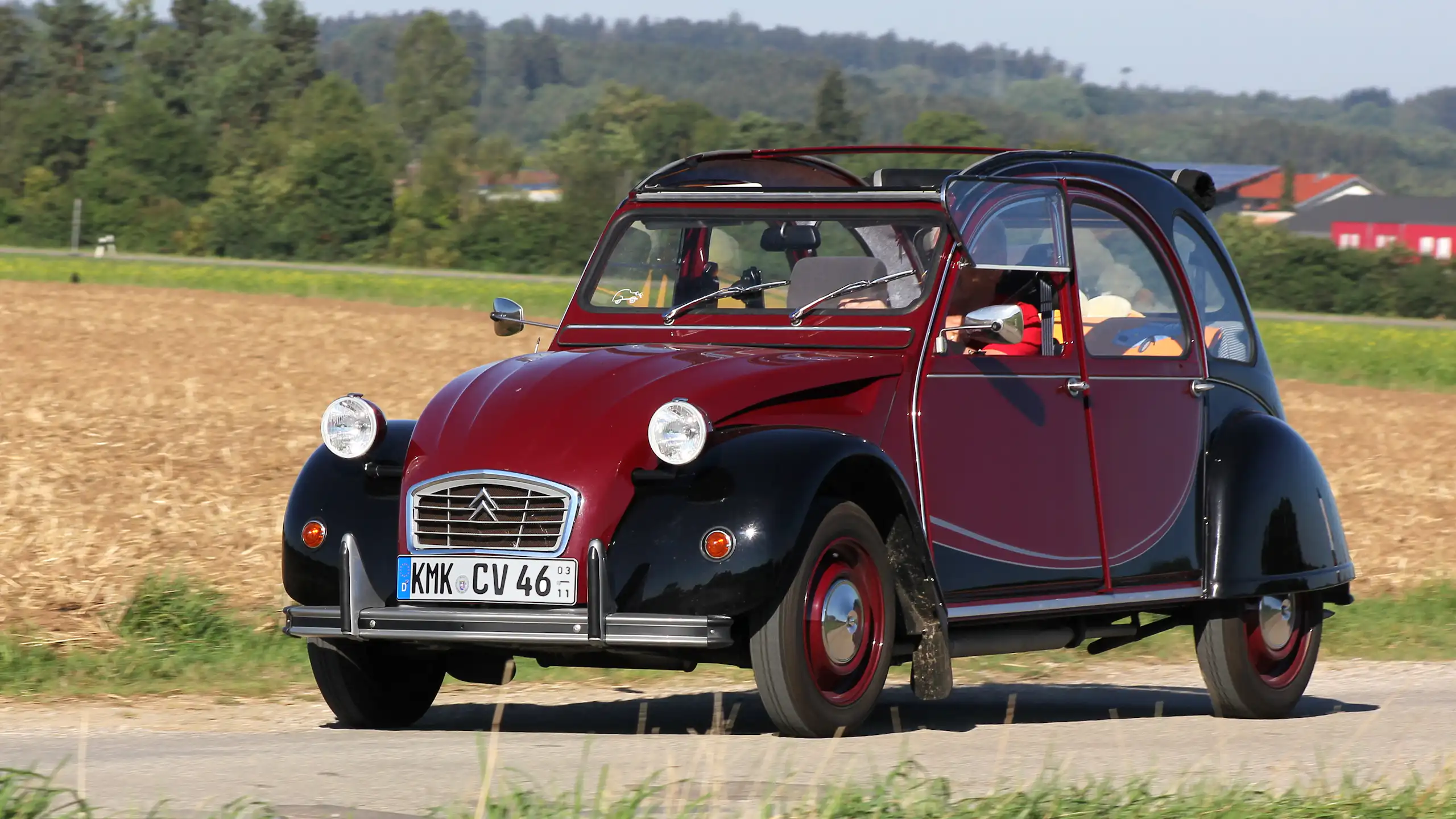 Deux chevaux Citroën modèle Charleston (bordeaux et noir) sur une route de campagne.