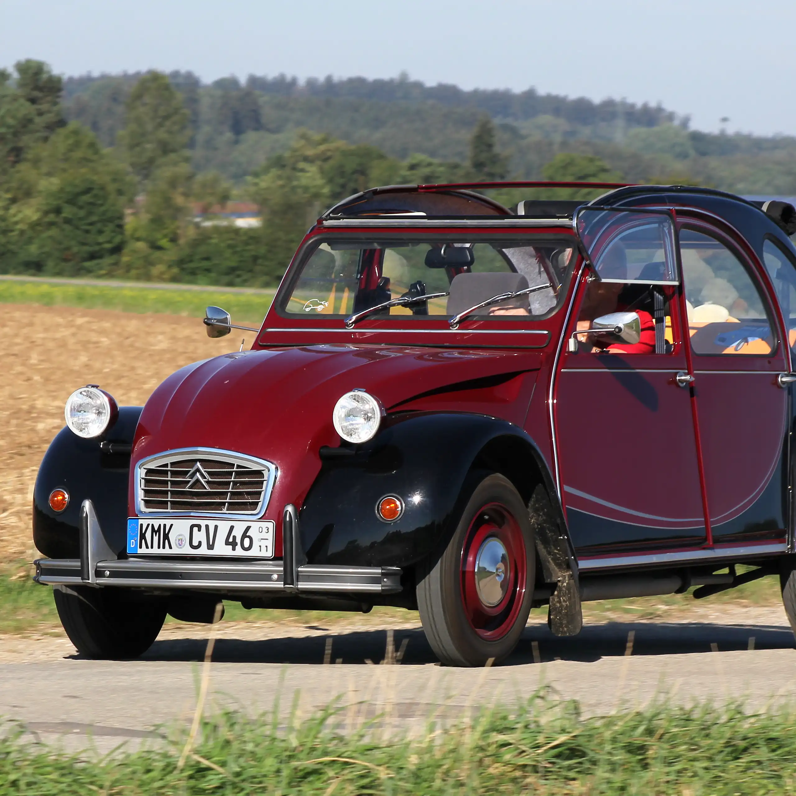 Deux chevaux Citroën modèle Charleston (bordeaux et noir) sur une route de campagne.