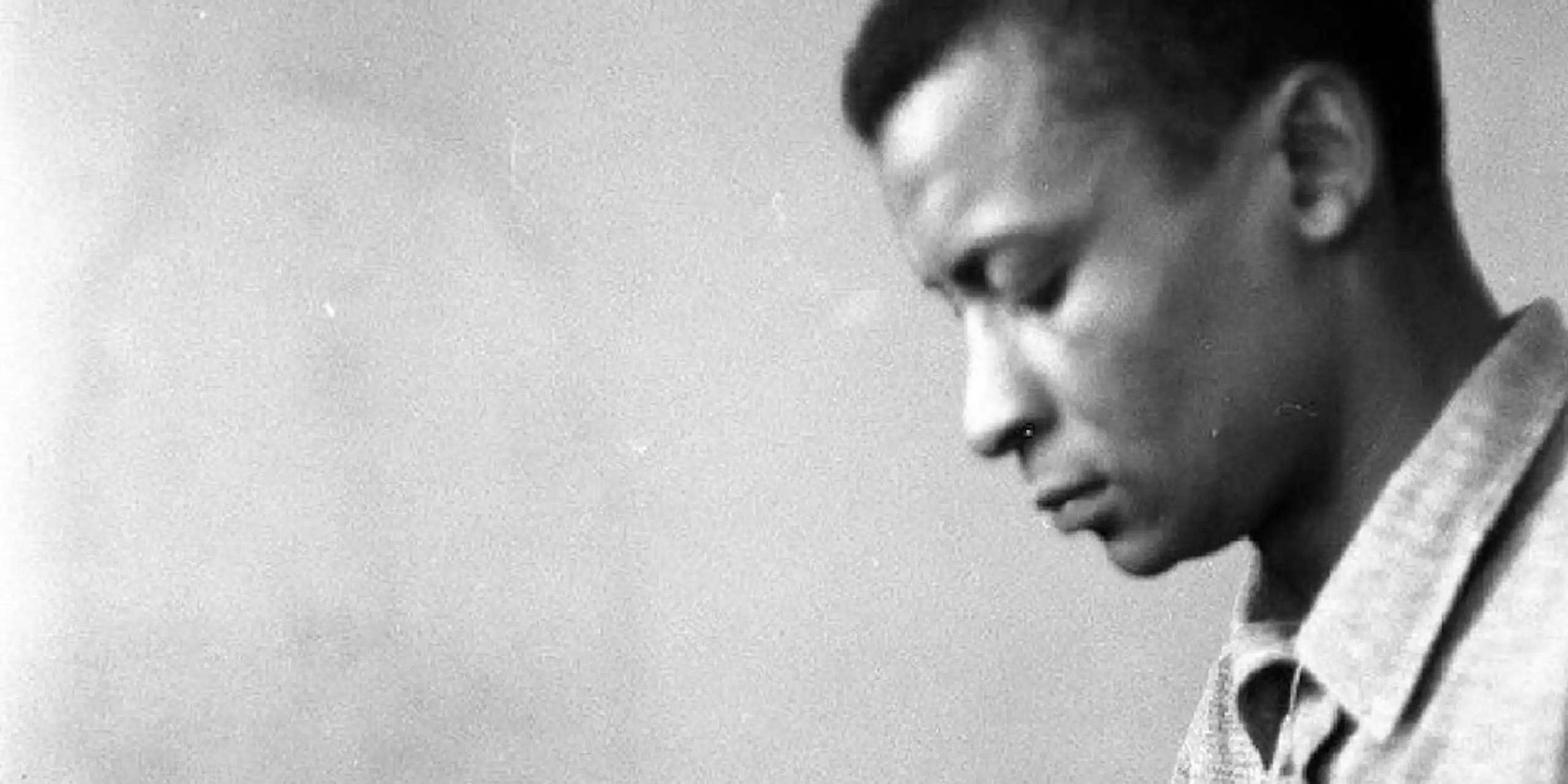 A moody black and white photo of a young African man in profile, looking downwards.