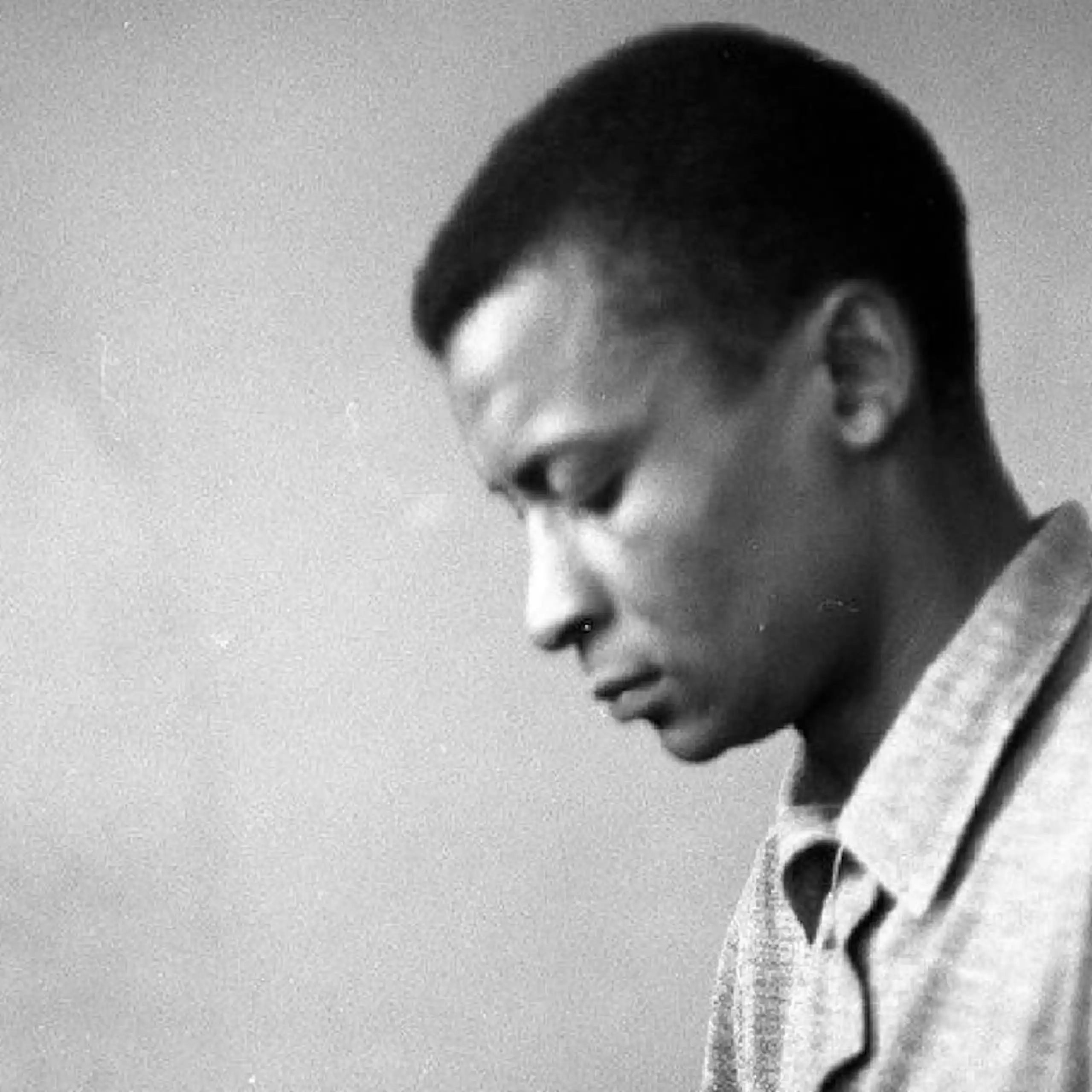 A moody black and white photo of a young African man in profile, looking downwards.