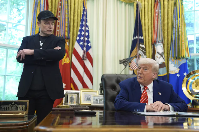 Elon Musk in black and a cap with Donald Trump in Oval Office