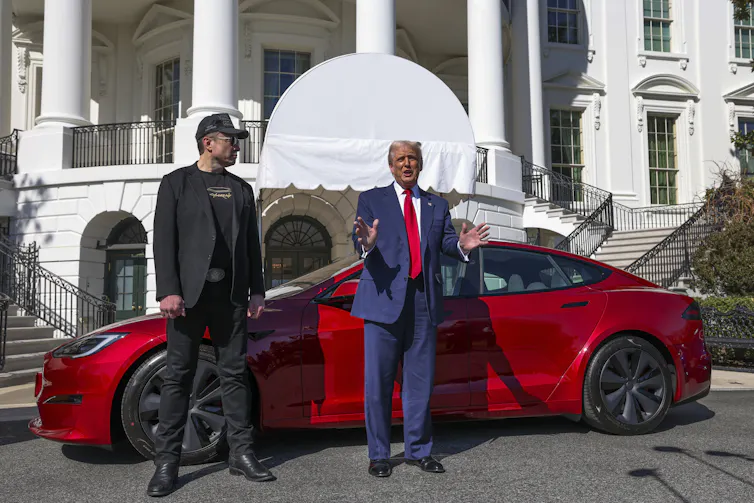 Black-clad Musk and Trump with a red Tesla car