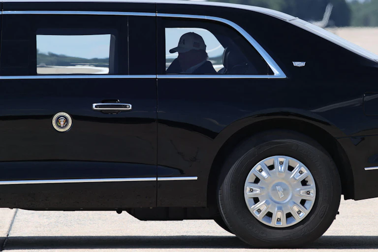 Donald Trump in a baseball cap seen through the windeow of his limousine, The Beast.