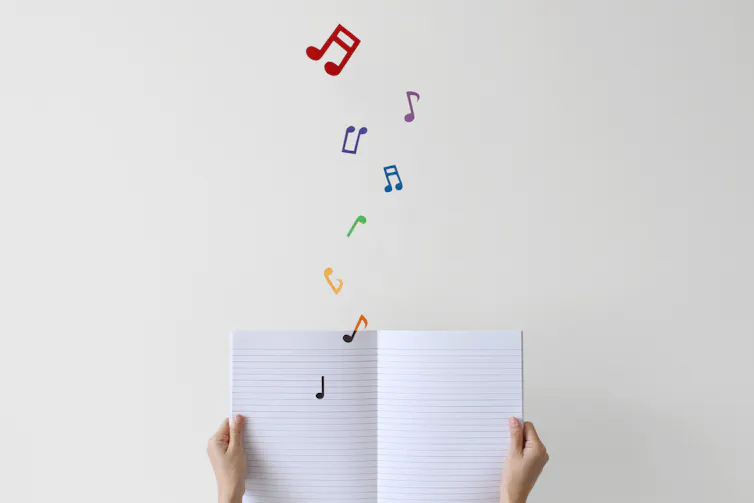 A person's hands are seen holding an open blank book that has music notes coming out of it.