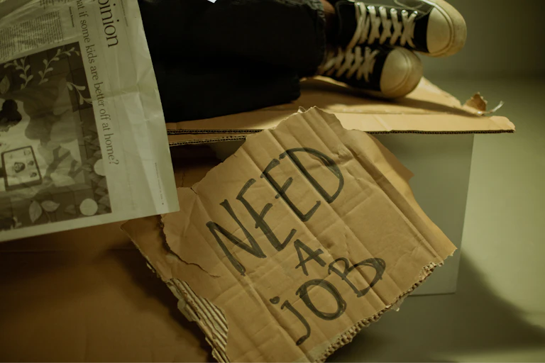 Piece of cardboard bearing the words "need a job"