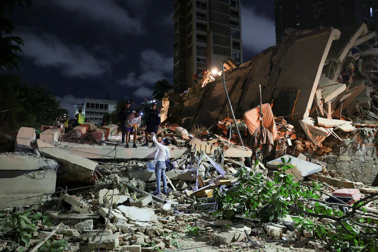 Varias personas sobre los escombros de un edificio por la noche
