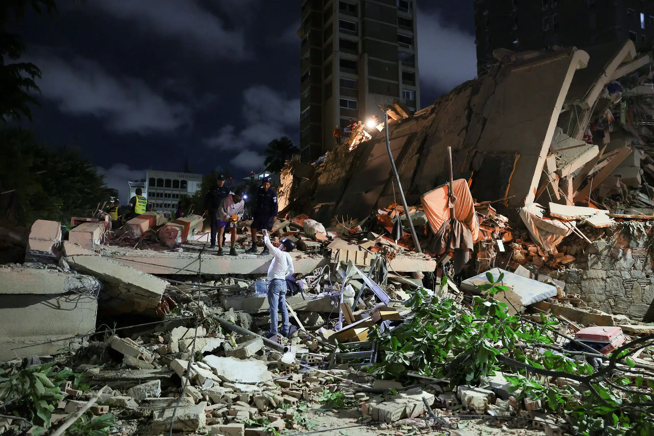 Varias personas sobre los escombros de un edificio por la noche