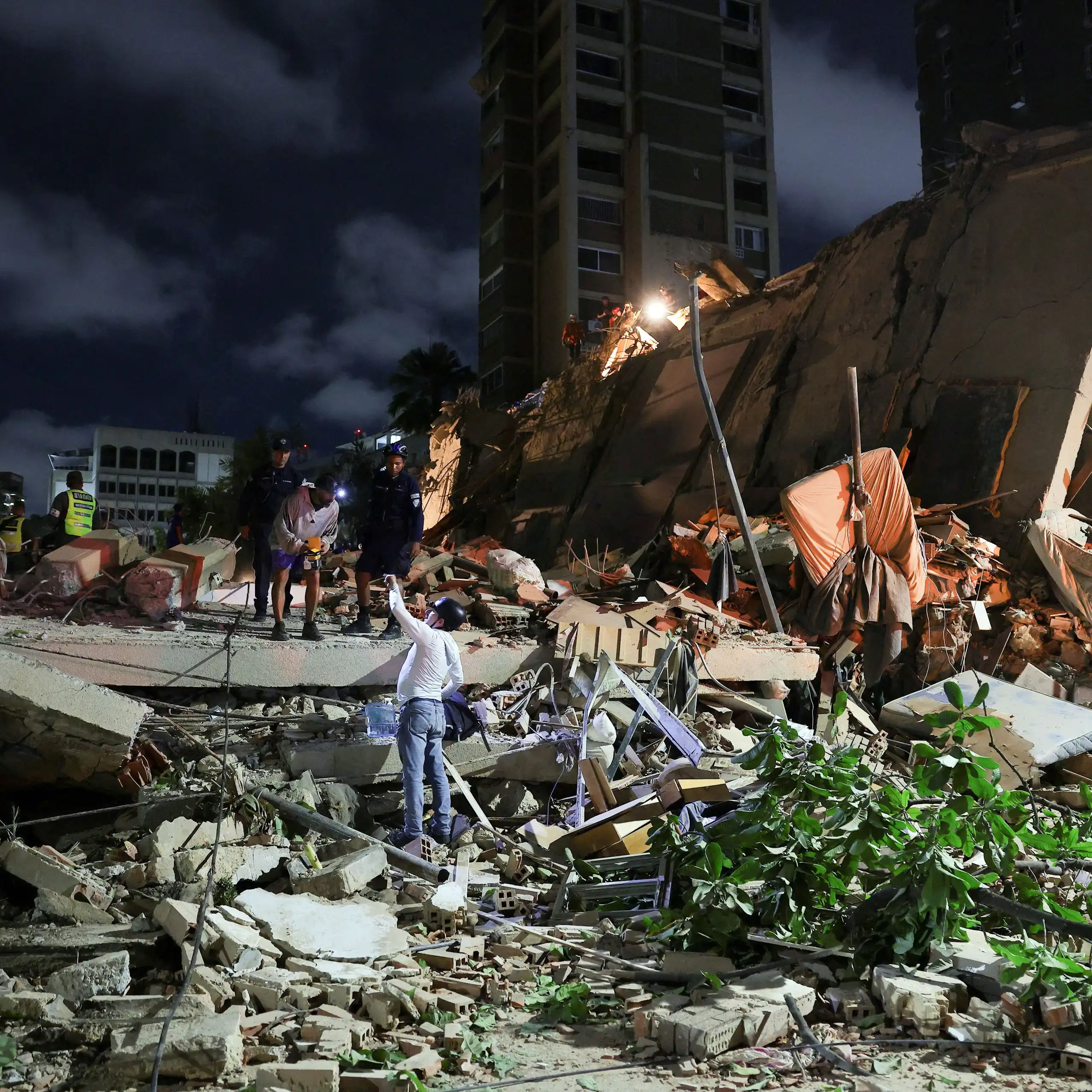 Varias personas sobre los escombros de un edificio por la noche