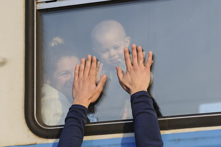Ukrainian refugees wave goodbye as they depart on a train.