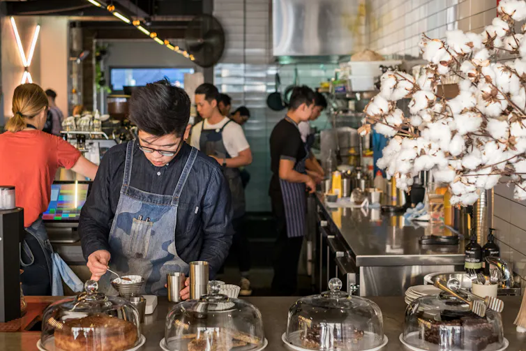 A man in glasses pours coffee in a commercial cafe kitchen