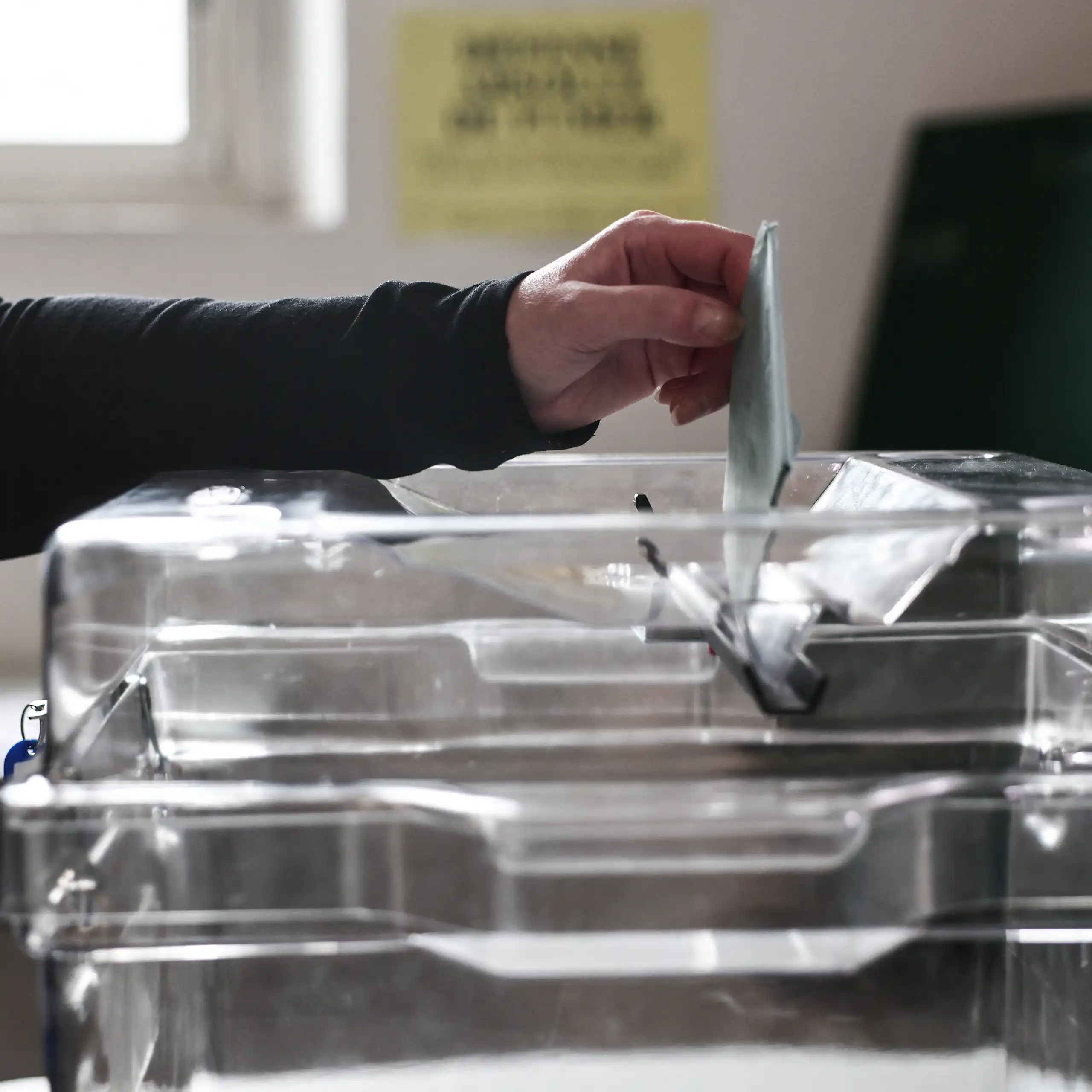 Close-up of a voter's hand casting a ballot into a ballot box.