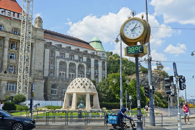 A large clock and thermometer in a city square during an intense heatwave. The thermometer reads 38 °C.