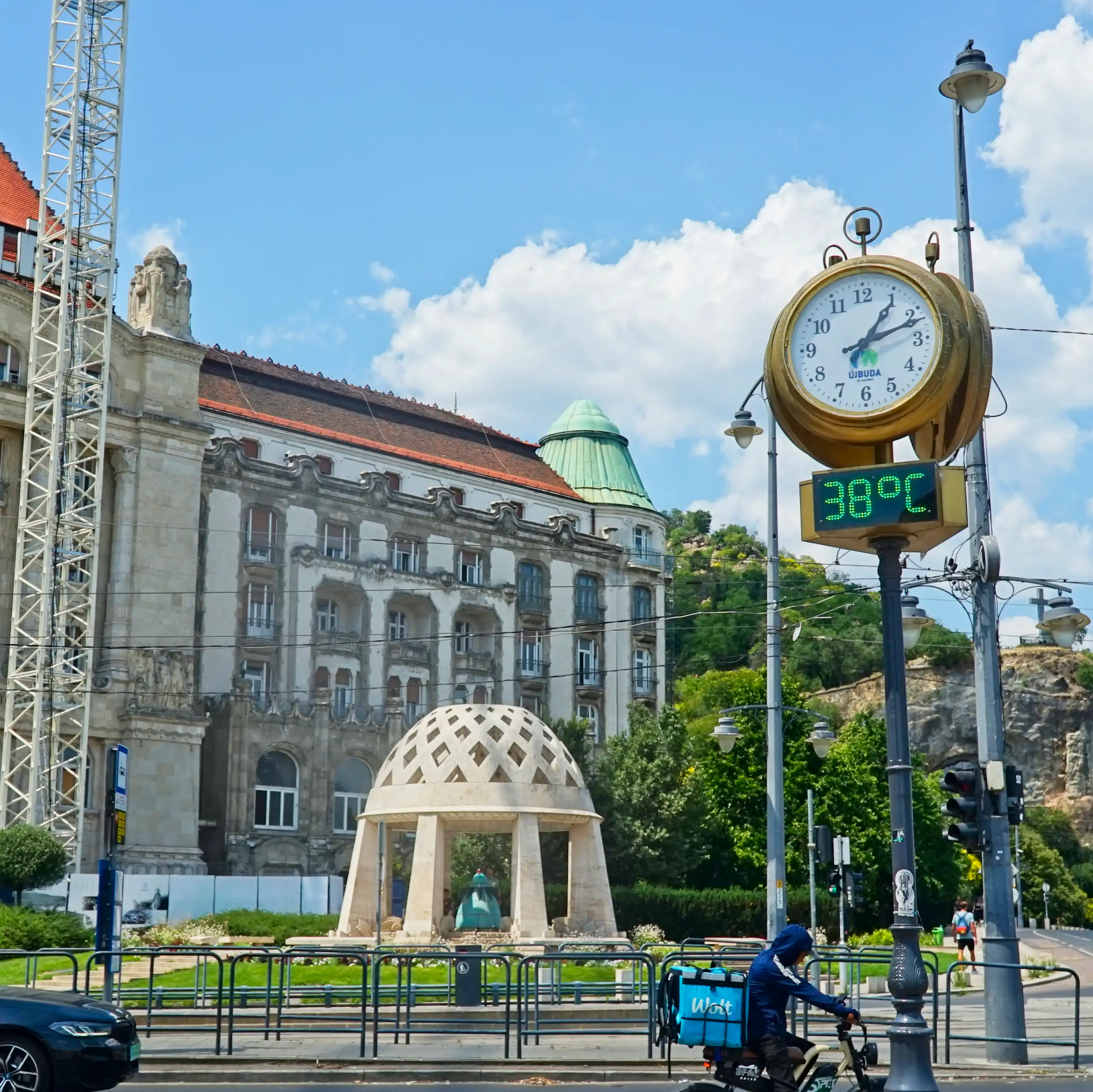 A large clock and thermometer in a city square during an intense heatwave. The thermometer reads 38 °C.