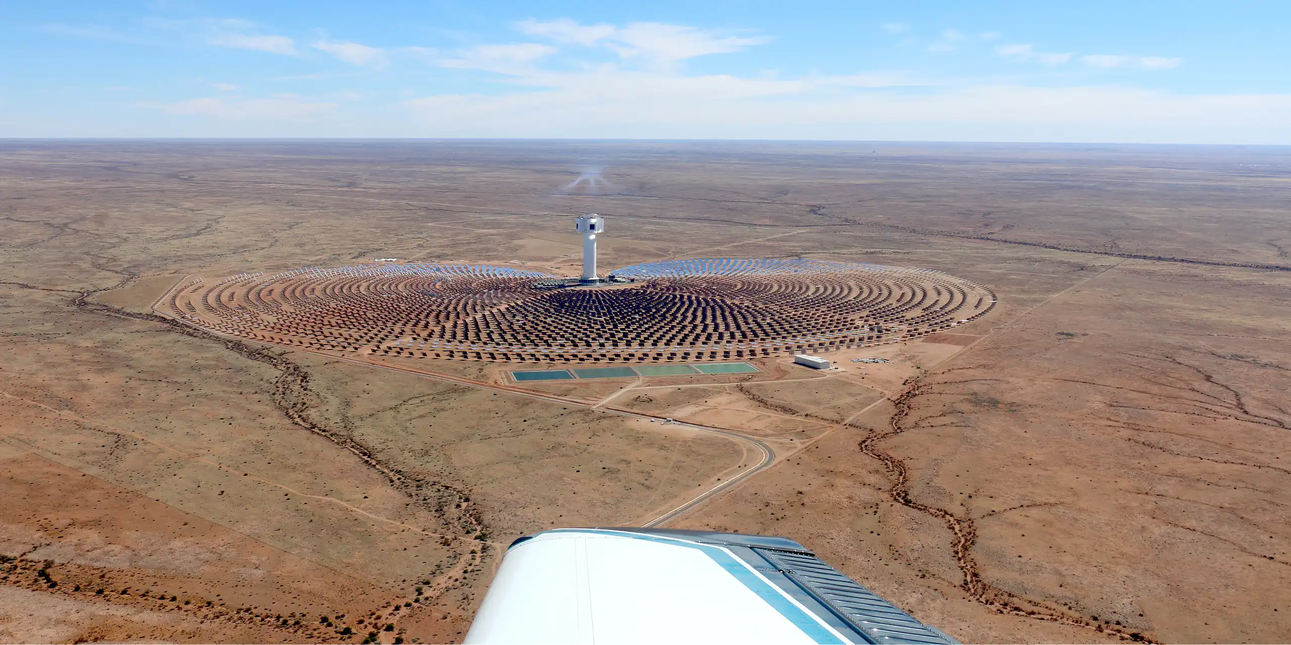 A solar plant seen from the sky - a tower in the middle with solar panels all around it.