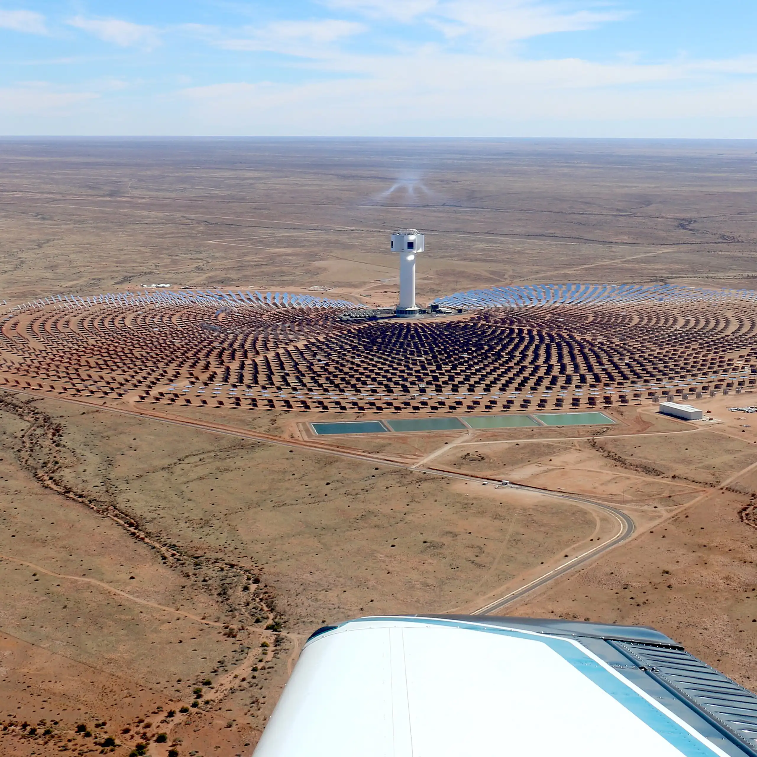 A solar plant seen from the sky - a tower in the middle with solar panels all around it.