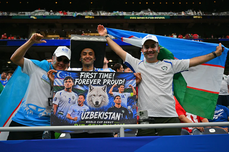 Two young man in a football stadium holding up a banner abut Uzbekistan's football team, the White Wolves.
