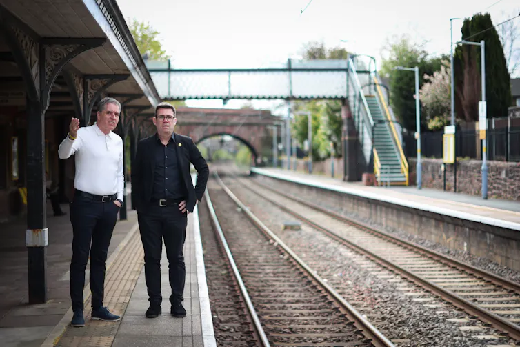 mayor of liverpool steve rotherham and andy burnham standing on a railway platform looking down the tracks.