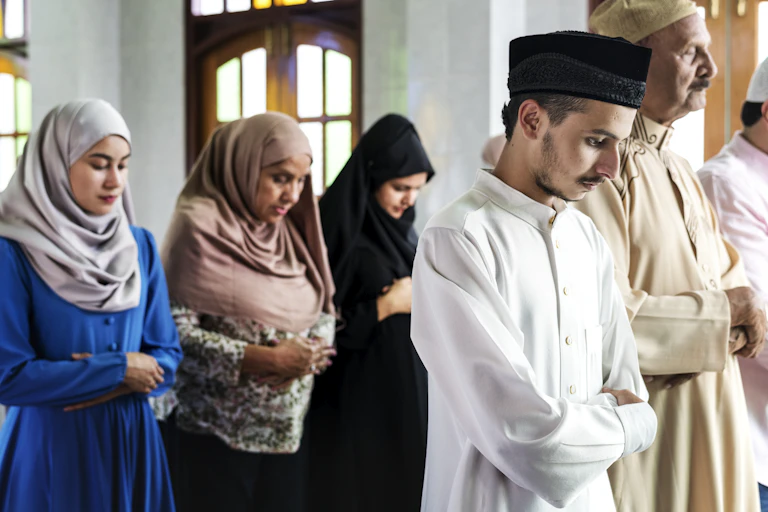 Men and women stand in separate rows, bowing their heads in prayer.