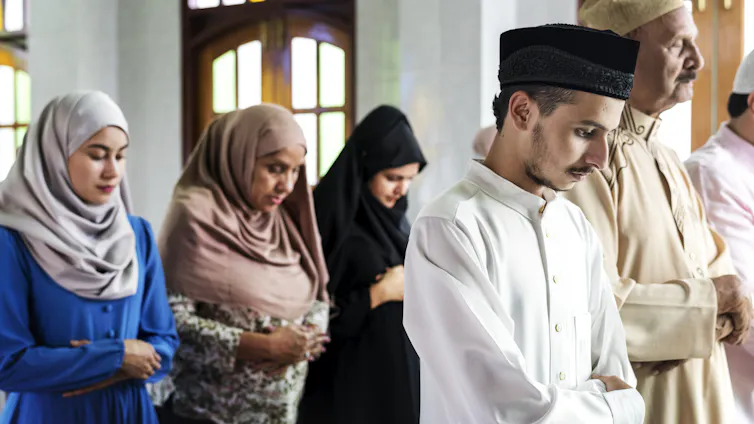 Men and women stand in separate rows, bowing their heads in prayer.