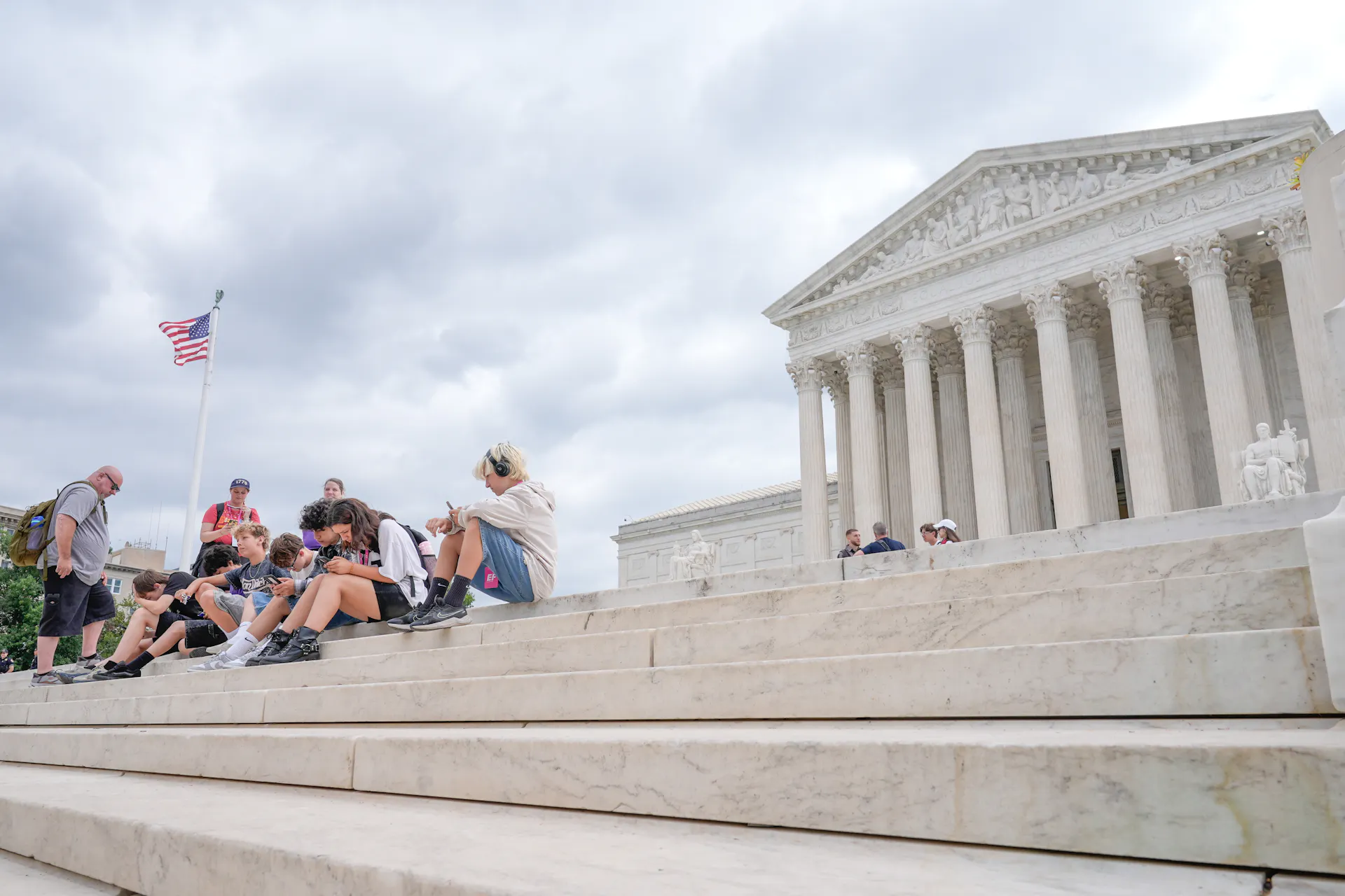 Several people sit on steps in front of a white federal building.