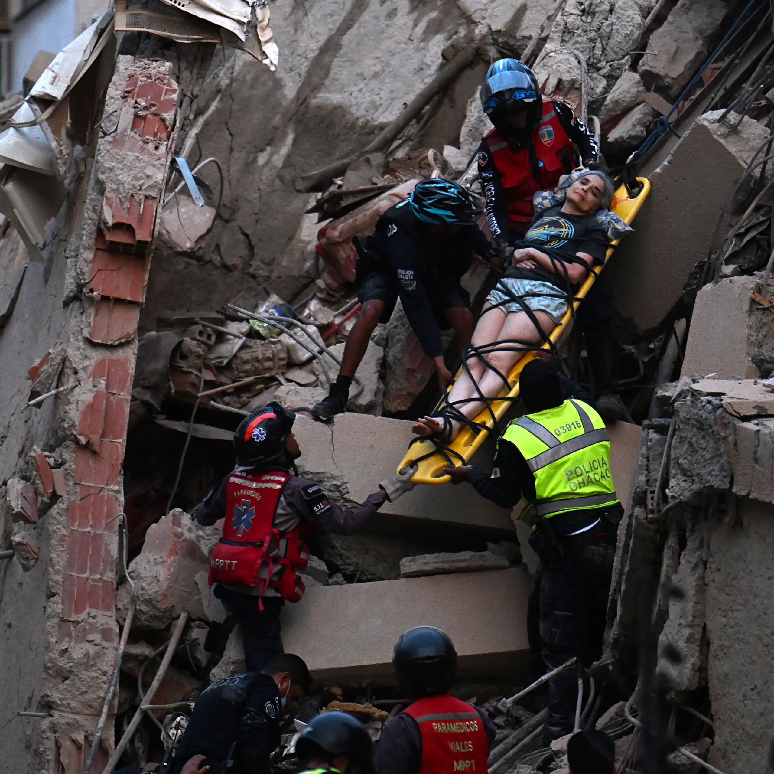 Aid workers rescue a woman strapped to a stretcher while descending a pile of rubble.