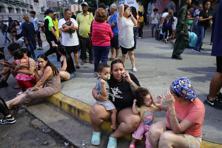 Large numbers of people speak by phone while sitting on curbs and milling around outdoors.